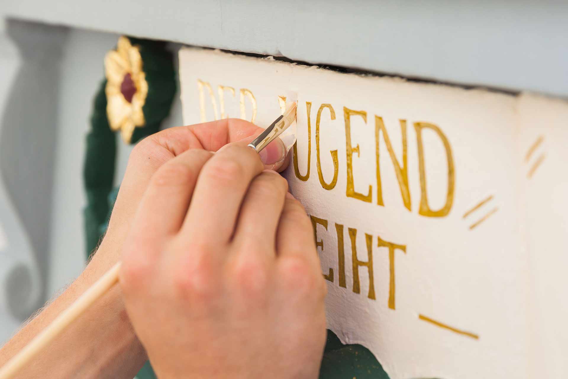 Mit dem Pinsel wird eine goldene Schrift gemalt